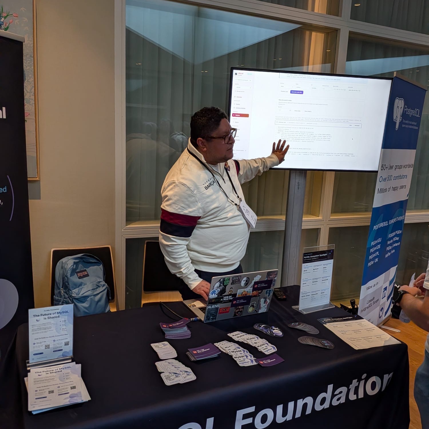 A presenter gesturing at a screen showing the dbtrail dashboard at the shared conference booth.